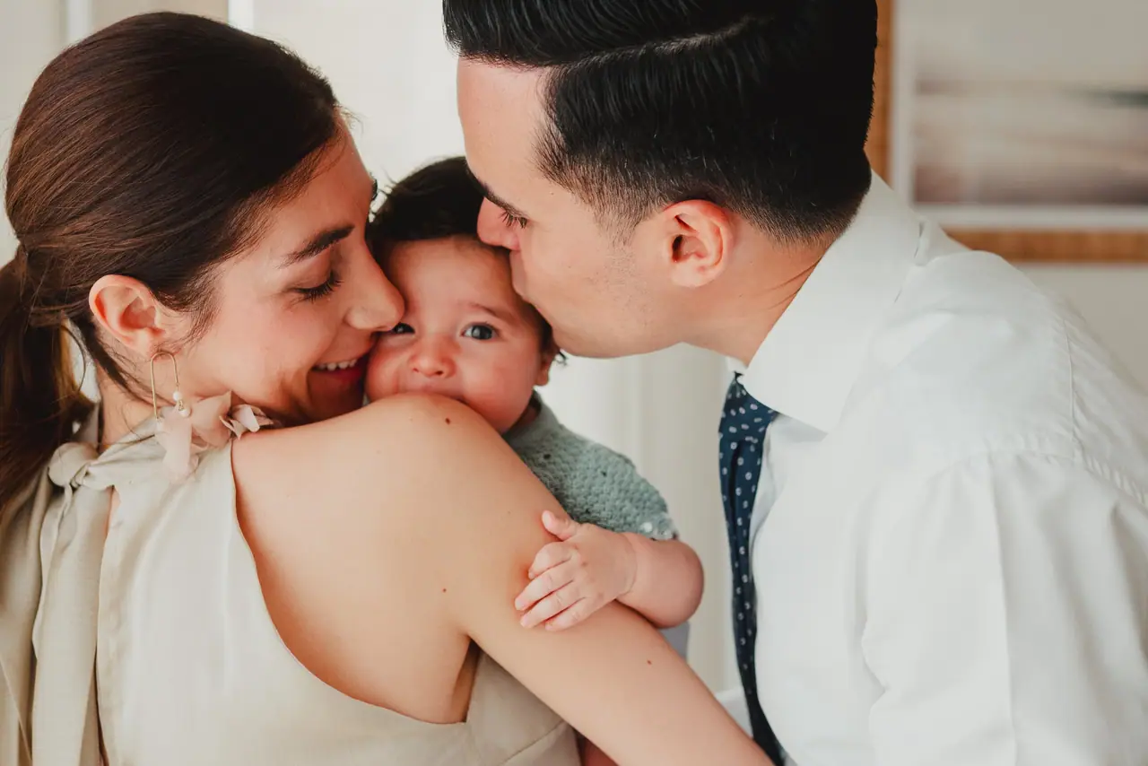 Fotografía de bautizo: padres beso bebe, en blanco y negro