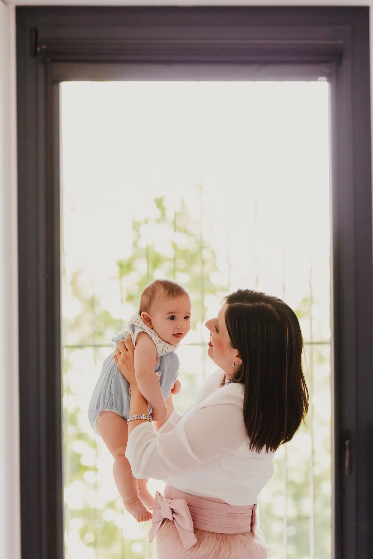 Fotografía de bautizo: madre levanta bebe ventana