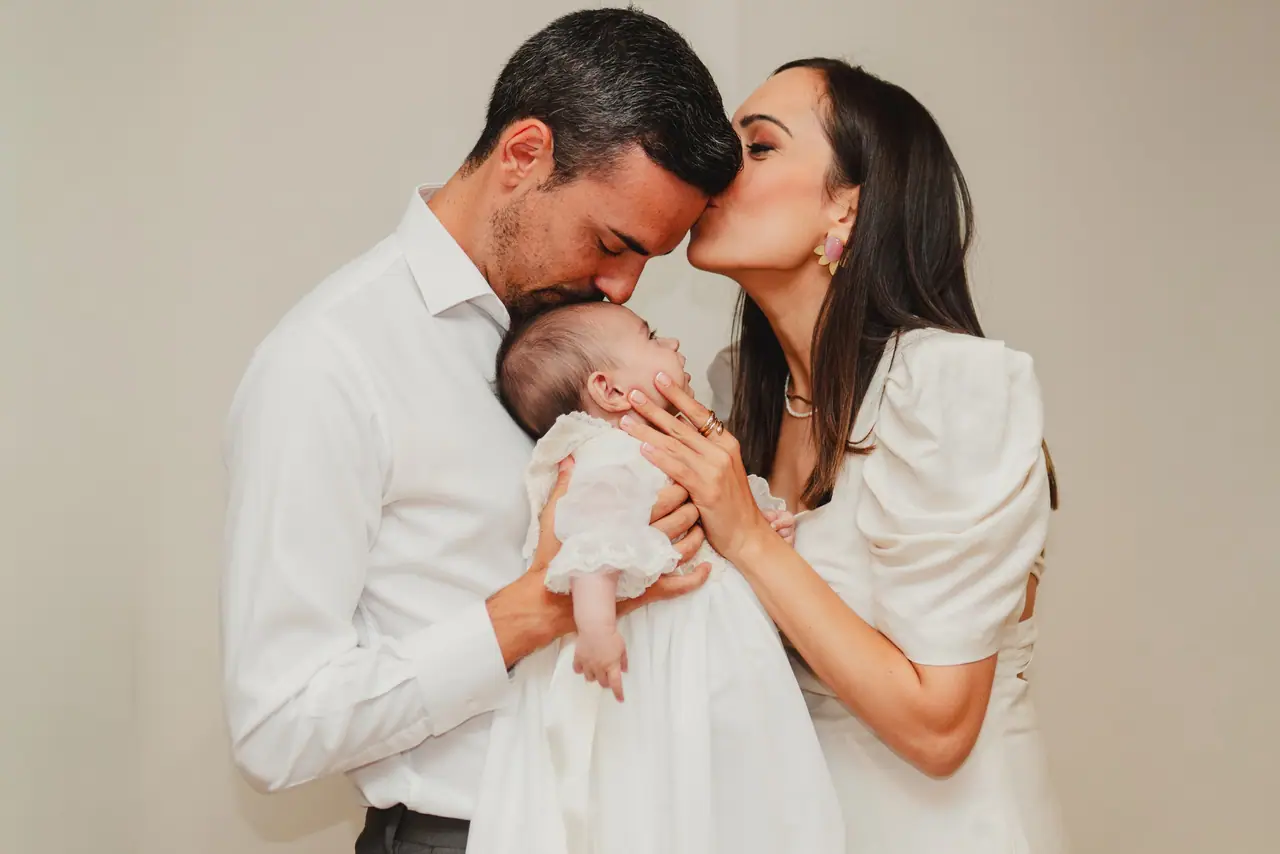 Fotografía de bautizo: padres beso bebe vestido blanco