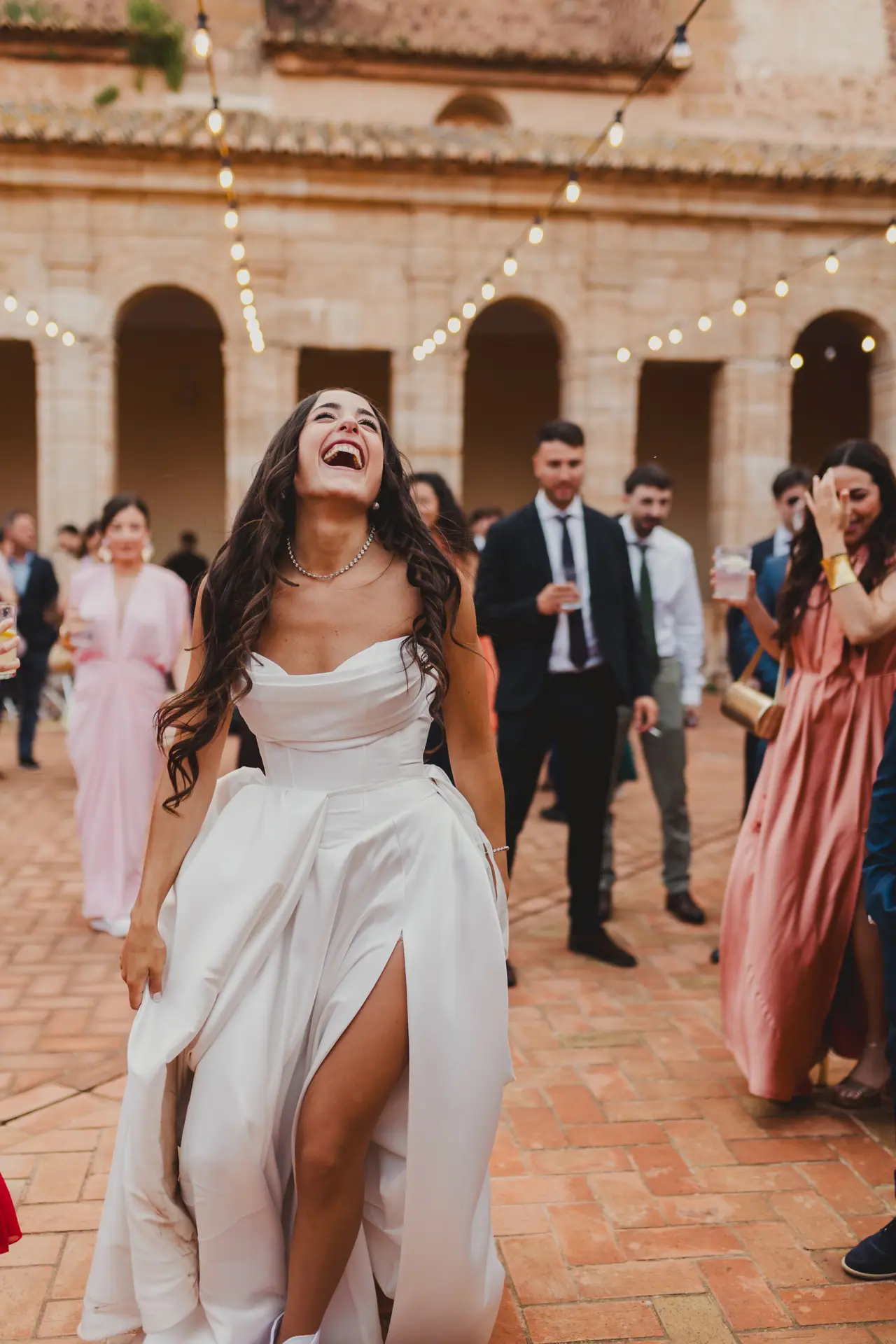 Fotografía de boda en Valencia: novia risa invitados en la Cartuja de Ara Christi, El Puig de Santa María