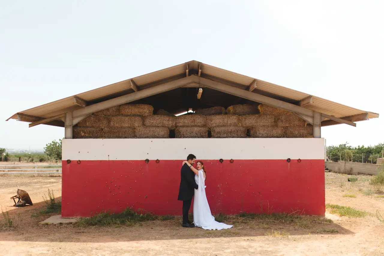 Novios besándose junto a un pajar rojo en el campo valenciano