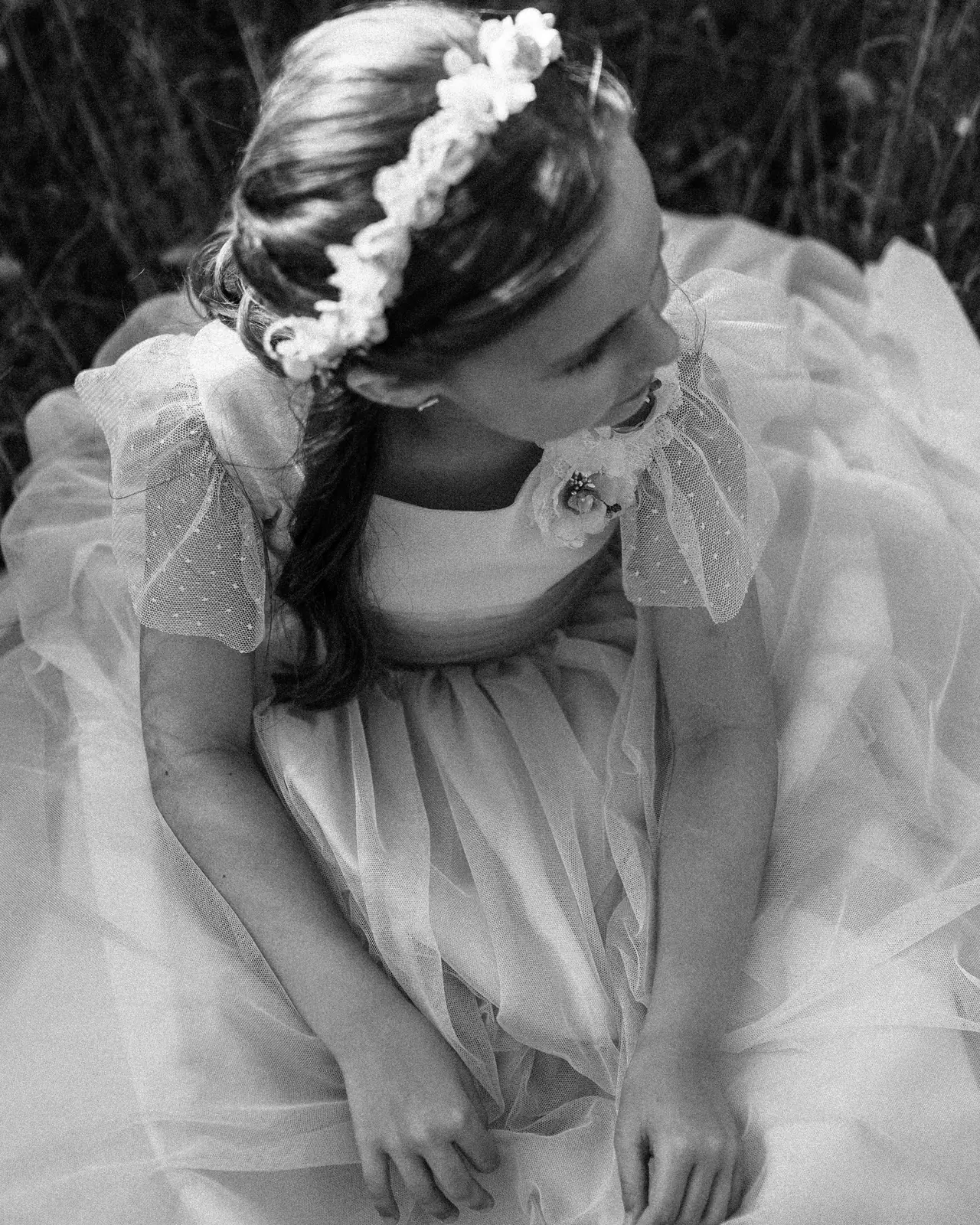 Niña con corona de flores mirando hacia abajo, en blanco y negro