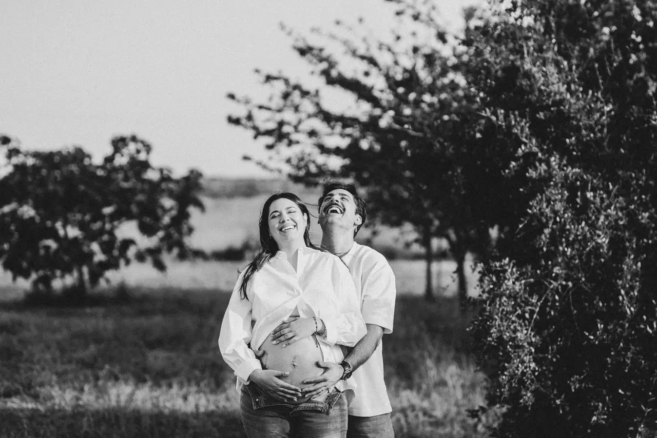 Pareja paseando entre árboles en su sesión de embarazo, en blanco y negro