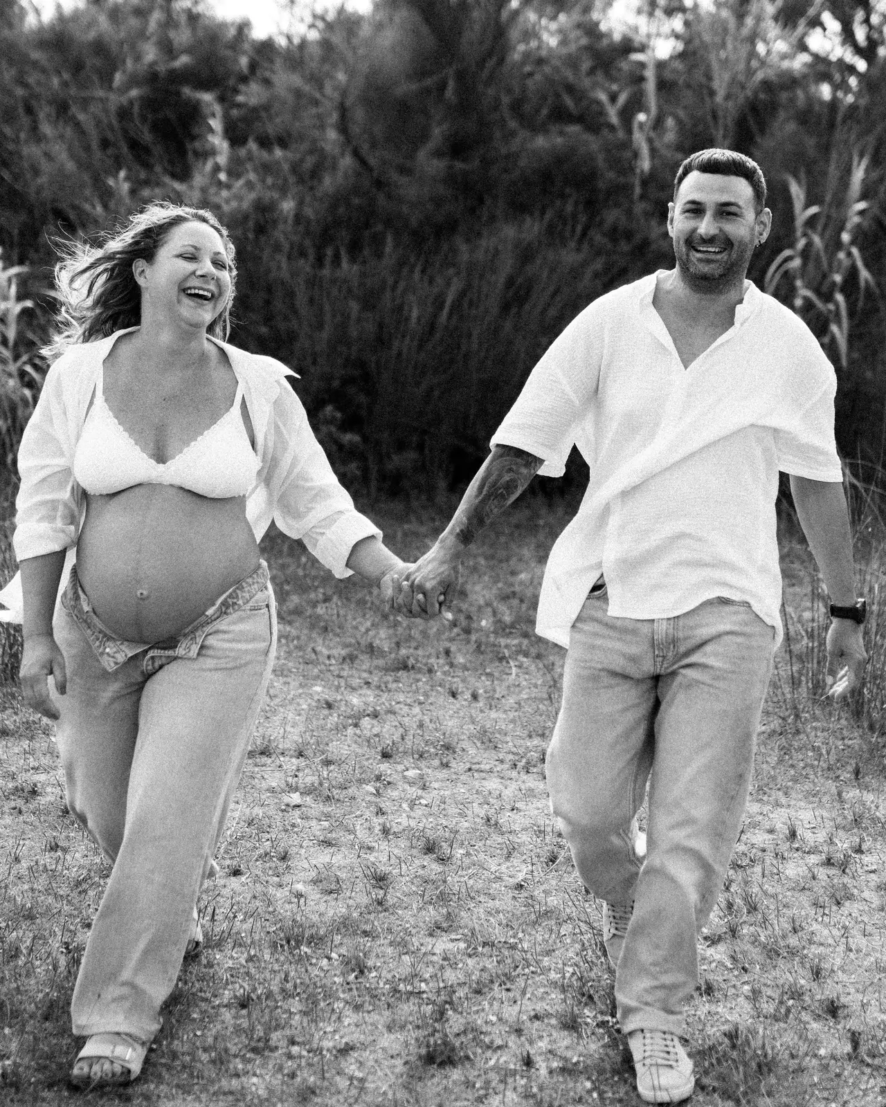 Pareja corriendo de la mano por el campo, sesión de embarazo en blanco y negro