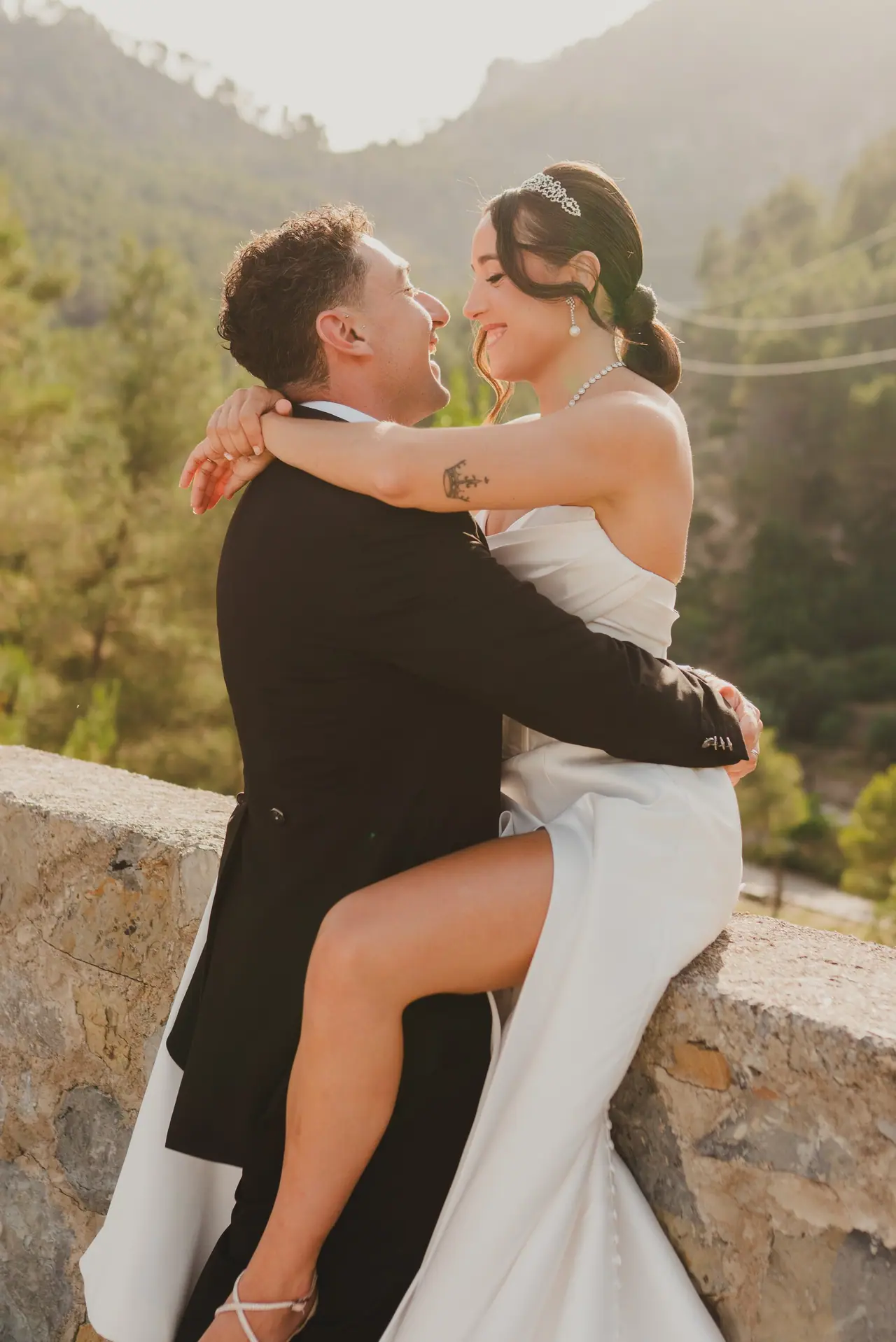 Novios mirándose sobre un muro de piedra con la montaña al fondo en su postboda